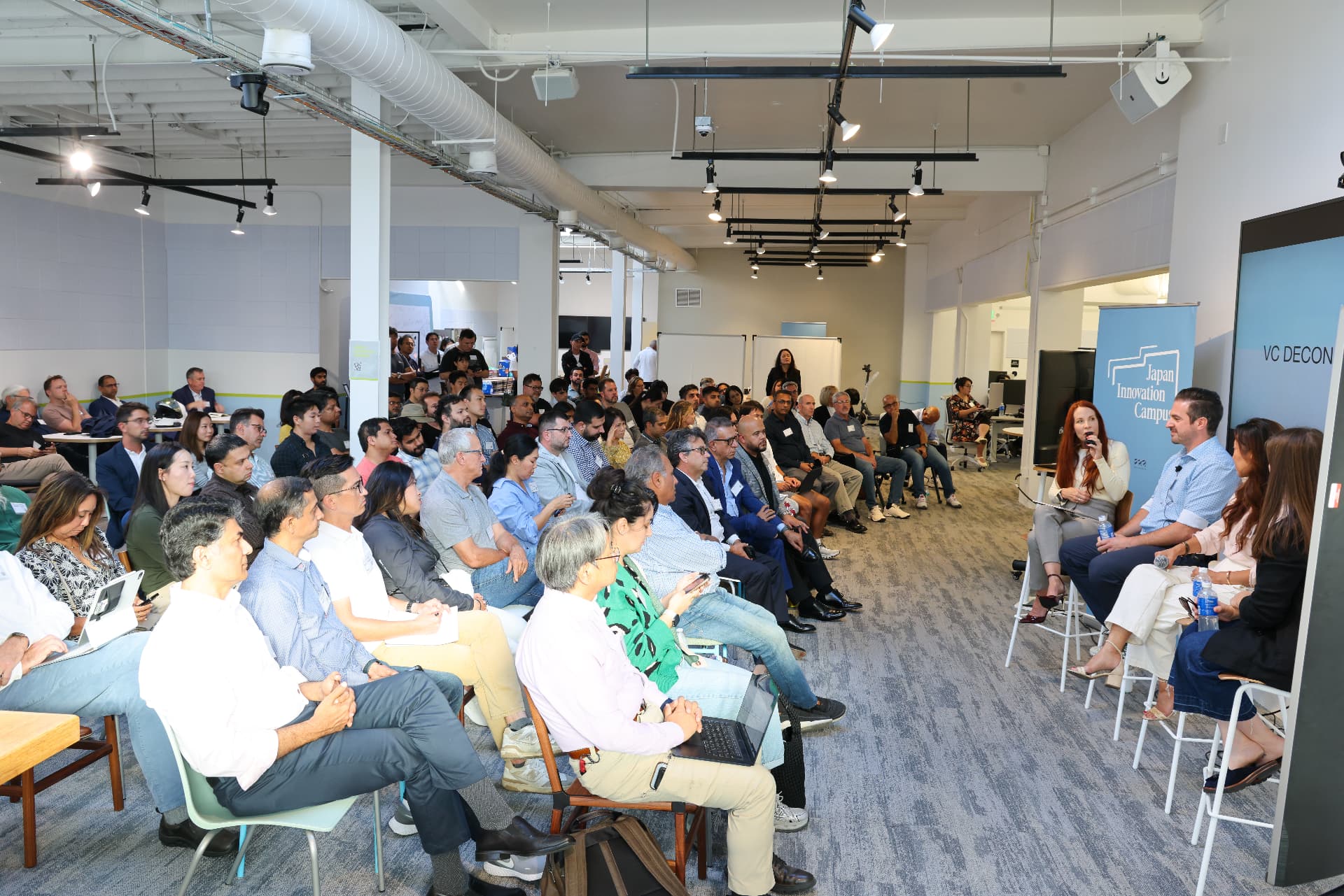 Annie Biggs moderating a panel discussion, microphone in hand, in front of a large live audience.