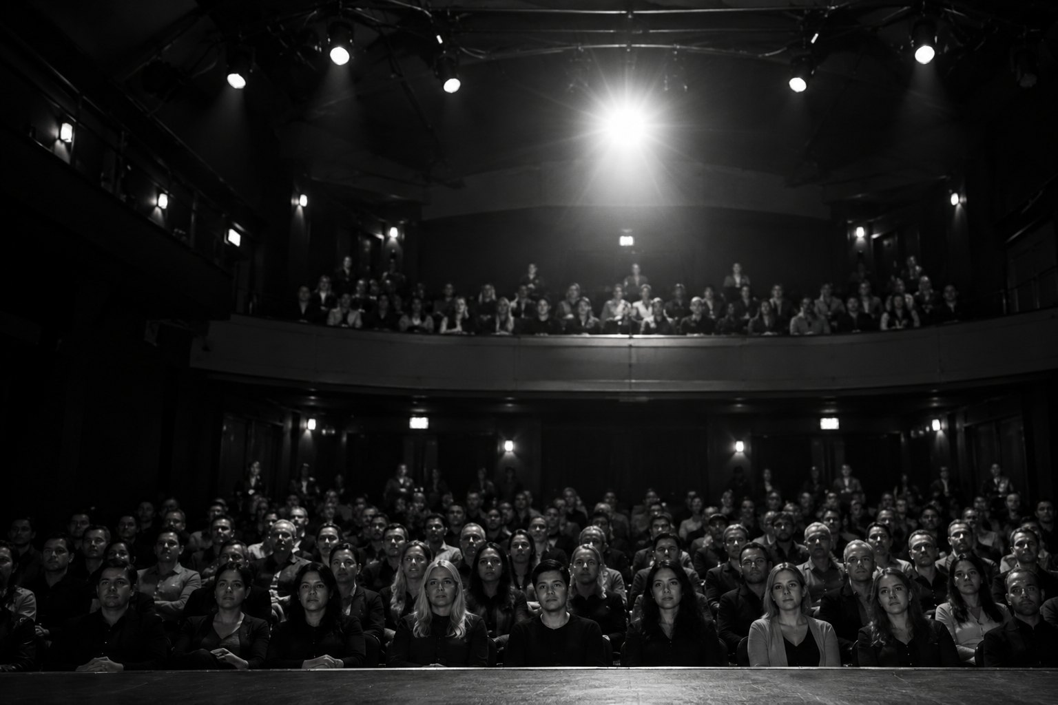 View from the stage into a darkened theater audience under a single overhead light